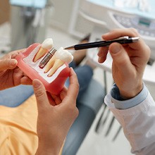 Dentist pointing at sample implant held by patient in light orange shirt