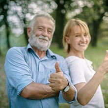 Mature couple standing outside, making thumbs up gesture