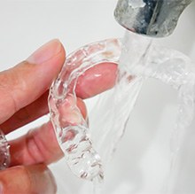 Closeup of fingers holding Invisalign under running water in a white sink