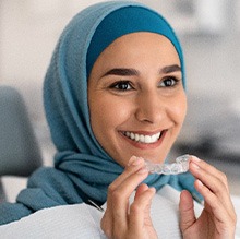 Woman in blue headwrap in dentist’s chair smiling holding Invisalign