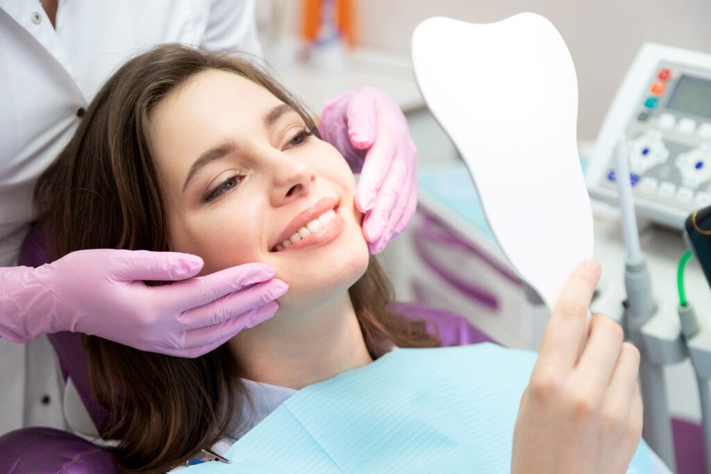 A woman smiling into a mirror at her dentist's office.